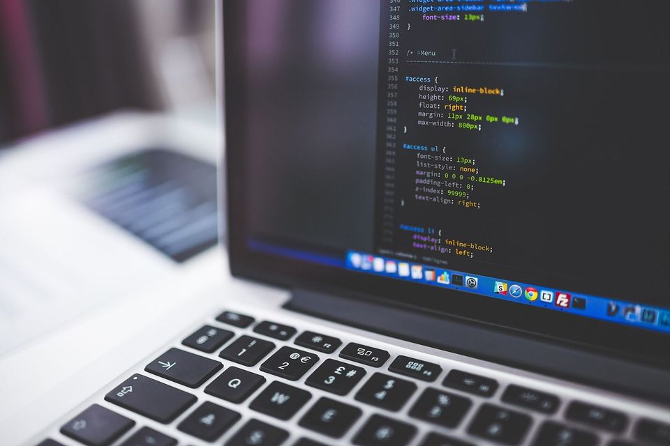 Laptop on a desk showing code in a dark editor theme