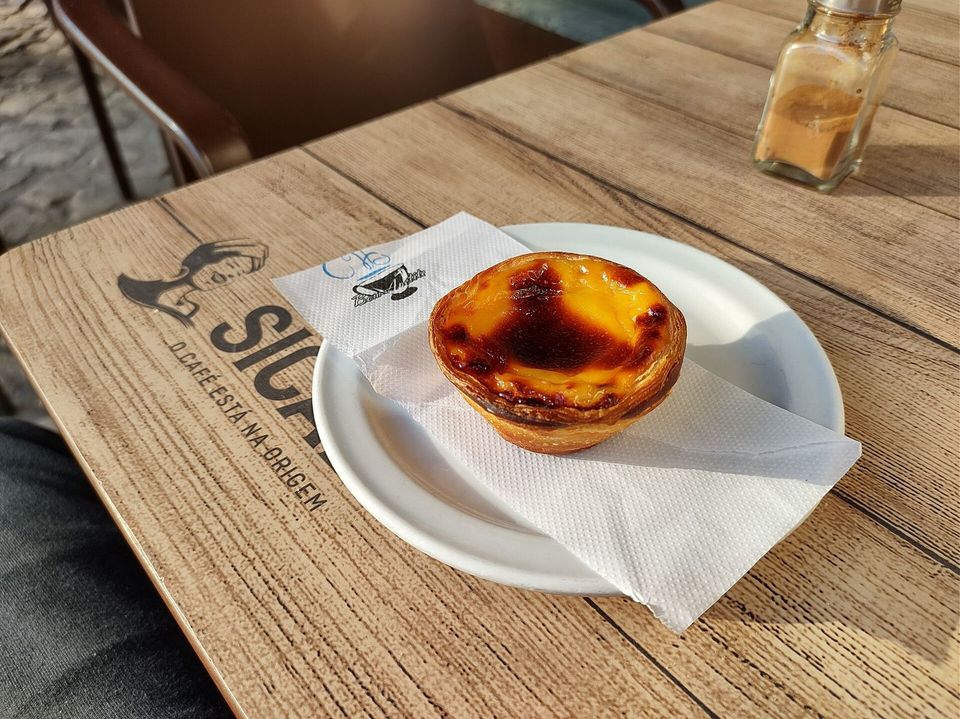 A pastel de nata on a saucer next to a coffee